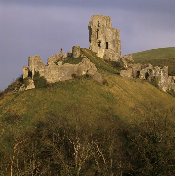 Corfe Castle ruins on top of a hill shrouded in orange light.